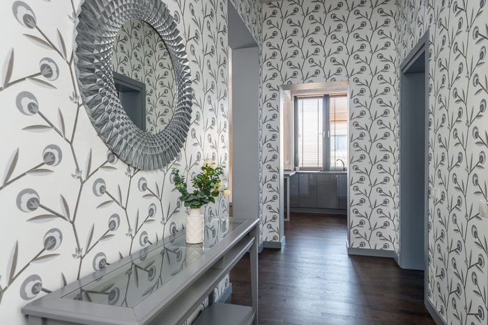 Hallway papered in a grey and white botanical print with a round silver mirror over a console table