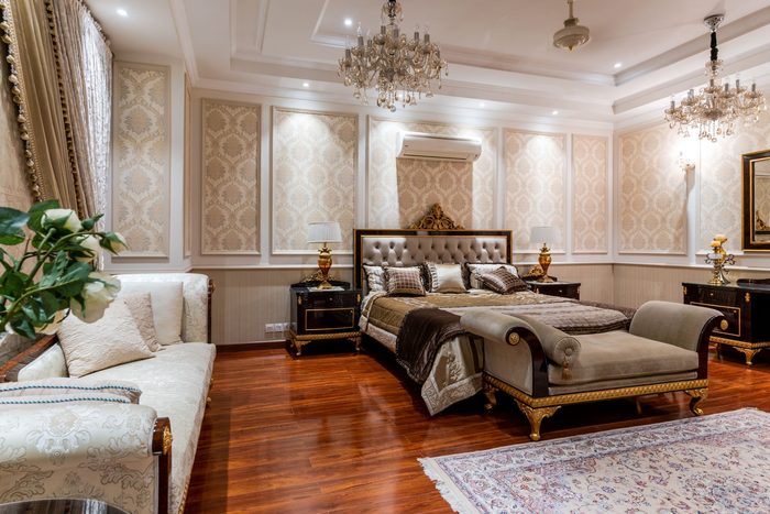 Spacious classic bedroom with cream damask wall panels, crystal chandeliers and a tufted bed