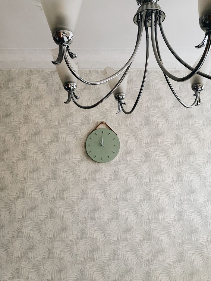 Pale grey fern-leaf wallpaper with a sage wall clock under a wrought-iron chandelier