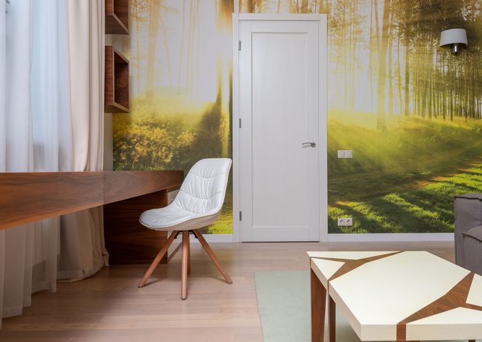 Home office with a sunlit birch-forest wall mural behind a wooden desk and white chair