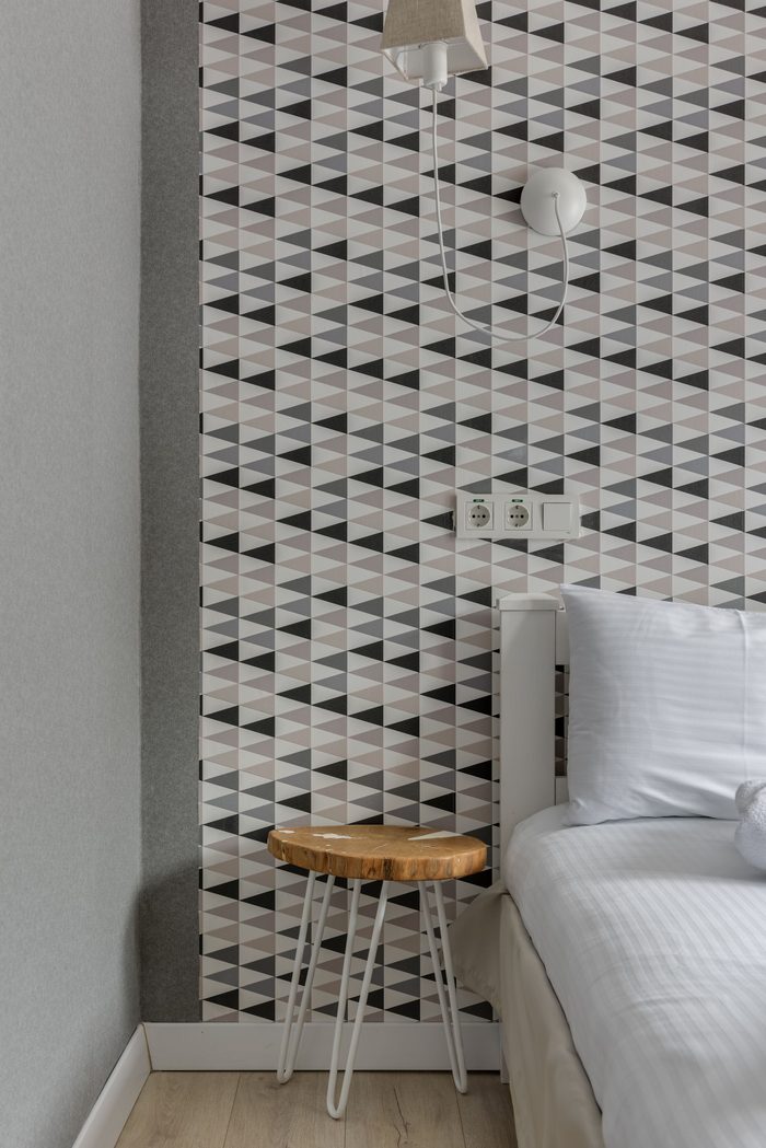 Narrow bedroom accent wall in a black, grey and white triangle wallpaper beside a wooden stool