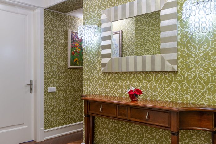 Entryway in an olive green scroll wallpaper with a wide striped mirror above a wooden console