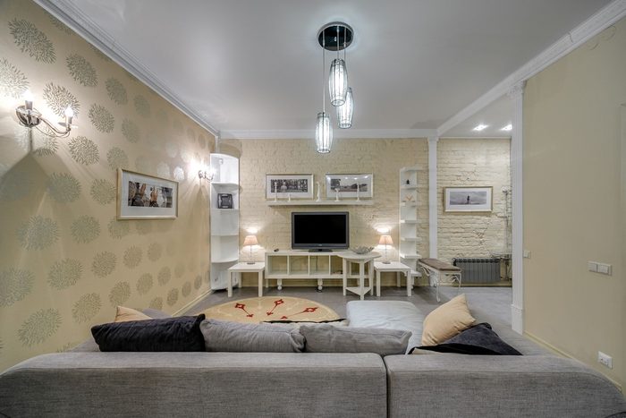 Open living room with a soft cream medallion wallpaper, a grey sectional sofa and glass pendant lights