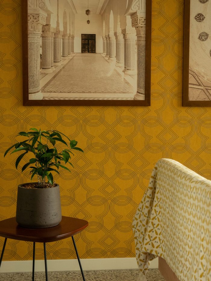 Ochre trellis-pattern wallpaper with framed architectural prints and a potted plant on a side table