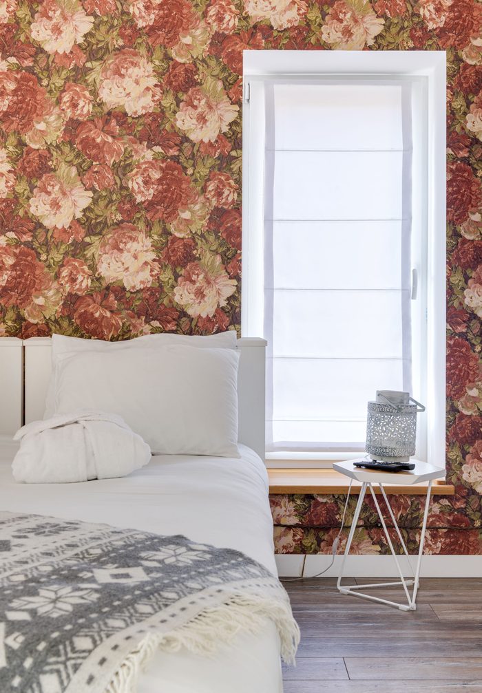 Bedroom with a large-scale red and pink rose wallpaper around a bright window and a white bed