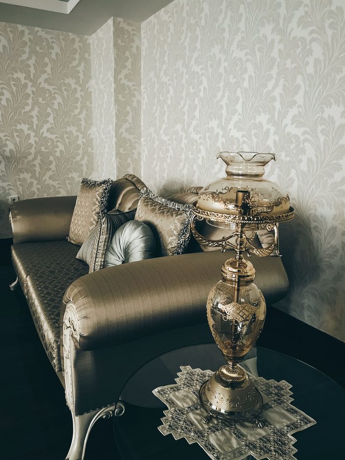 Silver satin chaise and ornate glass lamp in front of a pale silver damask wallpaper