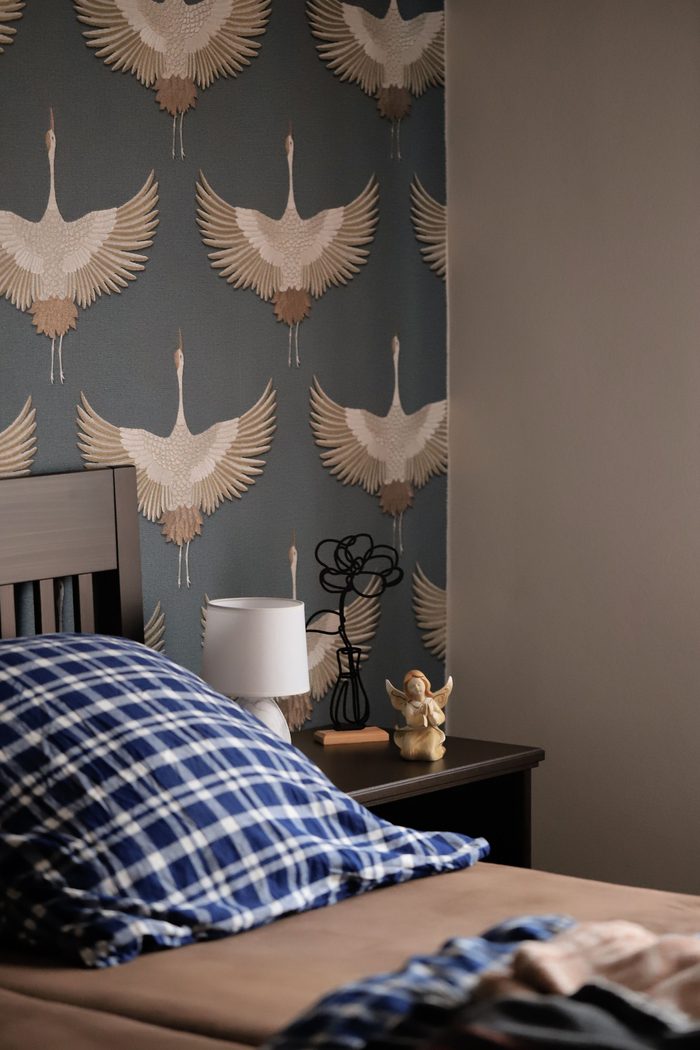 Bedroom feature wall with a slate-blue wallpaper of flying cranes above a wooden bed and a white table lamp